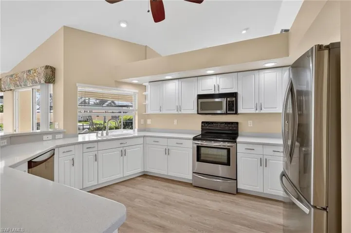 Kitchen featuring white cabinetry, stainless steel appliances, light-toned countertops, wood-finish flooring, and vaulted ceilings