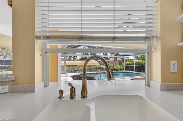 Kitchen sink with a gooseneck faucet, integrated basin, and speckled countertop, overlooking a screened-in pool and surrounding landscape