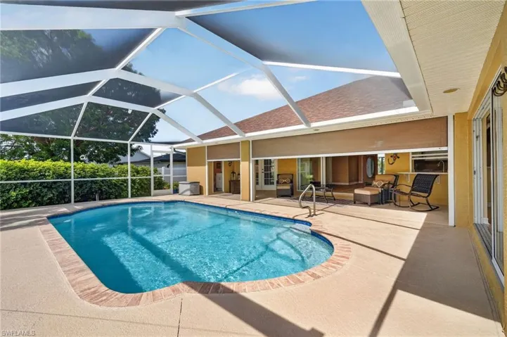 Screened-in pool area featuring a curved swimming pool with integrated steps and a handrail, surrounded by a concrete deck with a brick coping