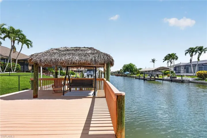 Expansive waterfront deck featuring a thatched-roof tiki hut, wood railing, and a water-facing swing