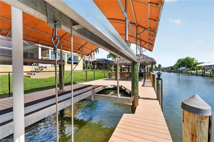 Waterfront property featuring a private boat lift with an orange canopy, a composite deck dock, and a built-in tiki hut