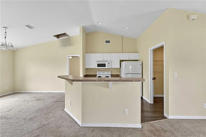 Open-concept kitchen and living area featuring vaulted ceilings, a breakfast bar with a laminate countertop, white cabinetry, and white appliances