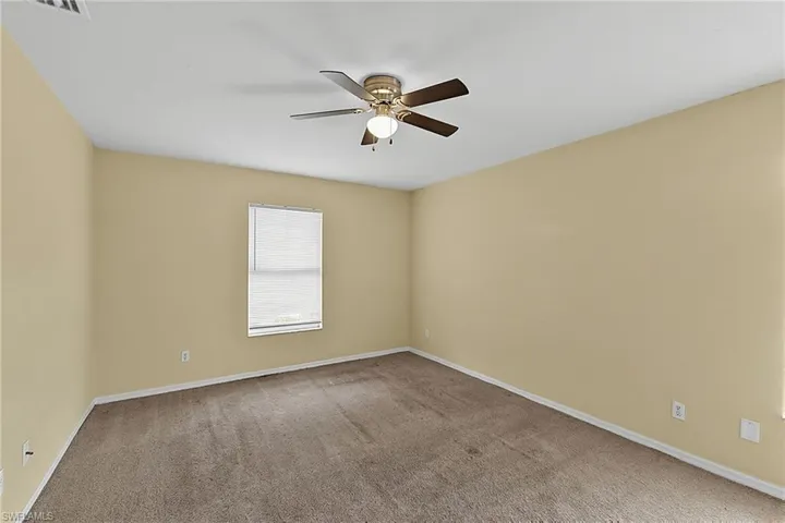 Spacious room featuring neutral carpeting, light beige walls, a window with horizontal blinds, and a ceiling fan with integrated lighting