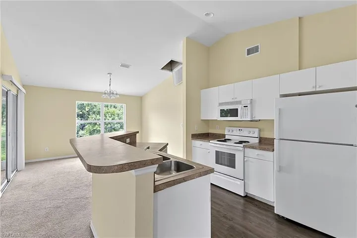 Open-concept kitchen featuring white cabinetry, a double basin stainless steel sink, and white appliances
