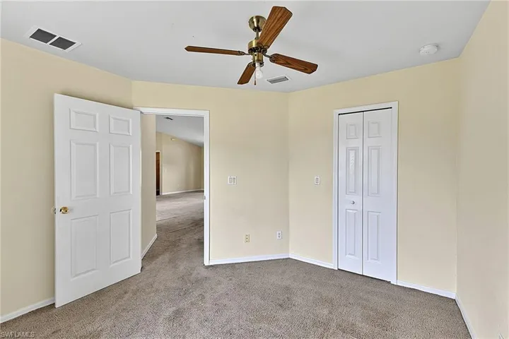 Carpeted room featuring a ceiling fan, light beige walls, a white bi-fold closet door, and a white six-panel door