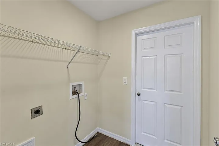 Utility room featuring a wire shelving unit, wood-finish flooring, and a six-panel door