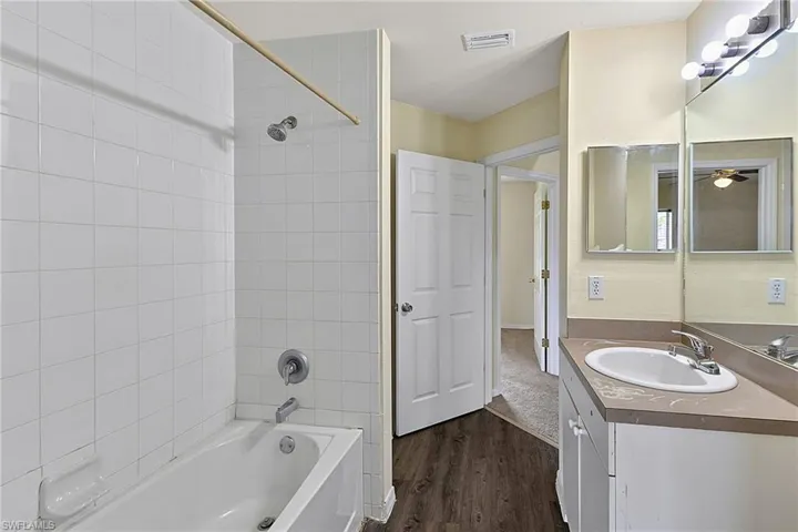 Bathroom featuring a white bathtub with subway tile surround, a single vanity with an integrated sink and light-toned countertop, and dark wood-finish flooring