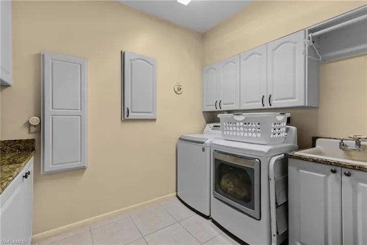 Oversized laundry area featuring washer and dryer, cabinets, sink, and light tile flooring
