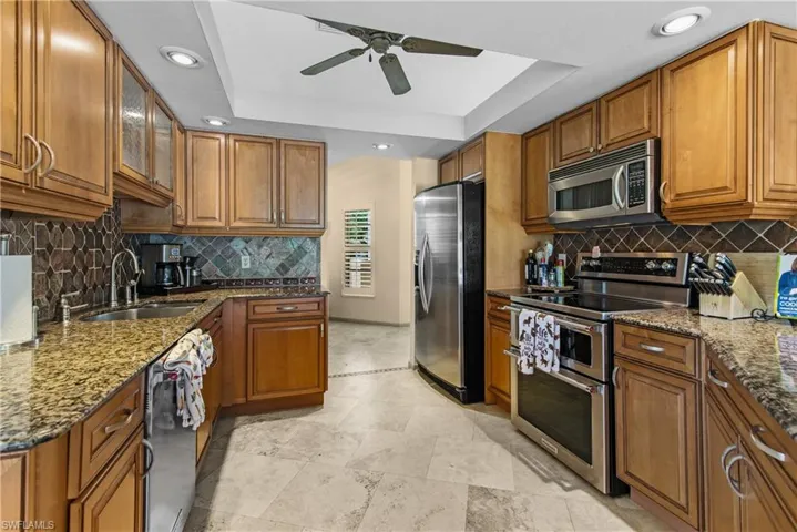 Kitchen with ceiling fan, light tile flooring, a raised ceiling, backsplash, and appliances with stainless steel finishes