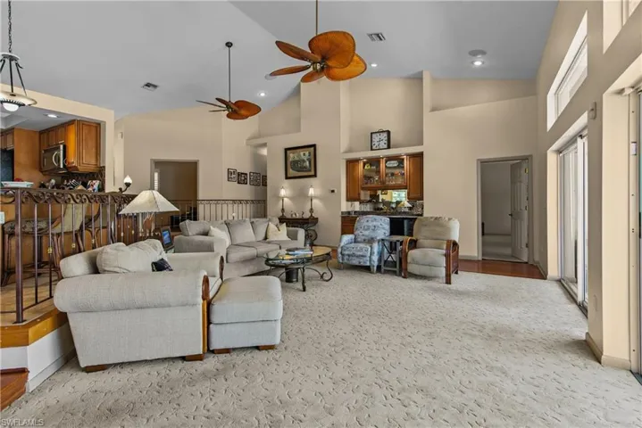 Entertainers living room with light carpet, high vaulted ceiling, ceiling fan, and built in bar