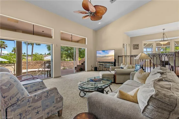 Living room with high vaulted ceiling, ceiling fan, carpet floors, and a healthy amount of sunlight