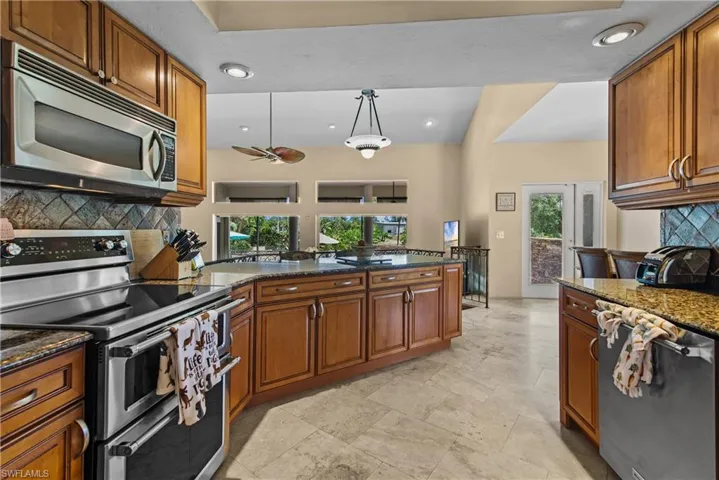 Kitchen with stone counters, kitchen peninsula, tasteful backsplash, light tile flooring, and appliances with stainless steel finishes