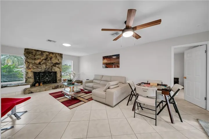 Living room with light tile patterned floors, a stone fireplace, and ceiling fan