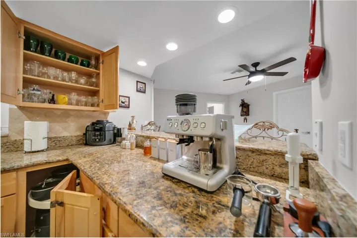 Kitchen with tasteful backsplash, light stone countertops, open shelves, recessed lighting, and light brown cabinets