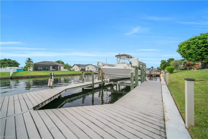 Dock area featuring boat lift, a water view, a yard, and a residential view
