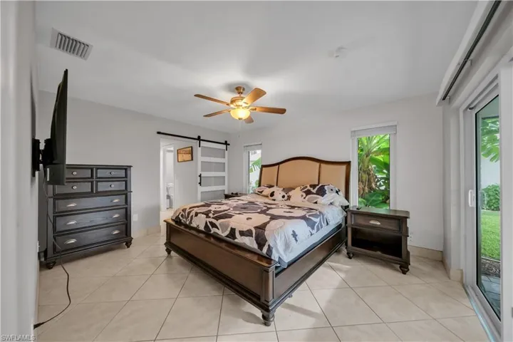Bedroom with access to outside, a barn door, light tile patterned floors, and a ceiling fan
