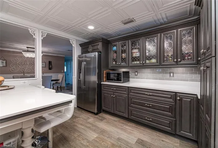 Kitchen with dark brown cabinetry, light hardwood / wood-style floors, decorative backsplash, appliances with stainless steel finishes, and ornamental molding
