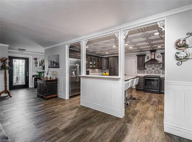 Kitchen with appliances with stainless steel finishes, dark hardwood / wood-style flooring, dark brown cabinetry, wall chimney range hood, and a kitchen island