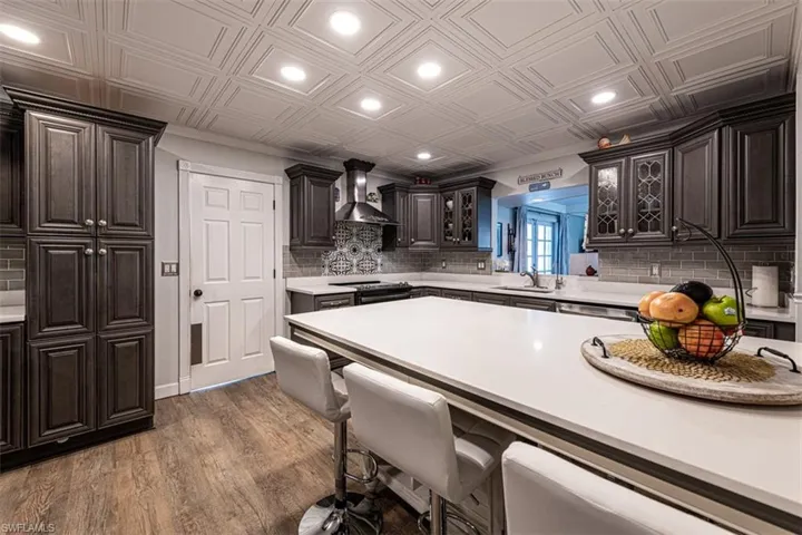 Kitchen with electric stove, sink, wall chimney exhaust hood, dark hardwood / wood-style flooring, and dark brown cabinetry