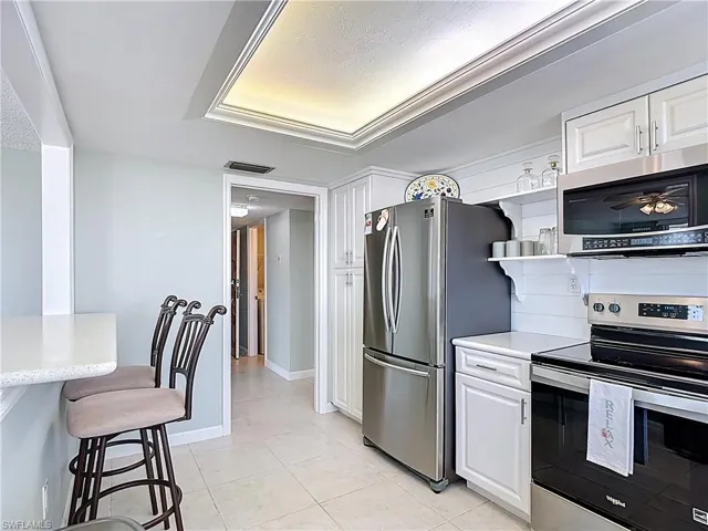Kitchen featuring stainless steel appliances, light countertops, white cabinetry, light tile patterned flooring, and a breakfast bar