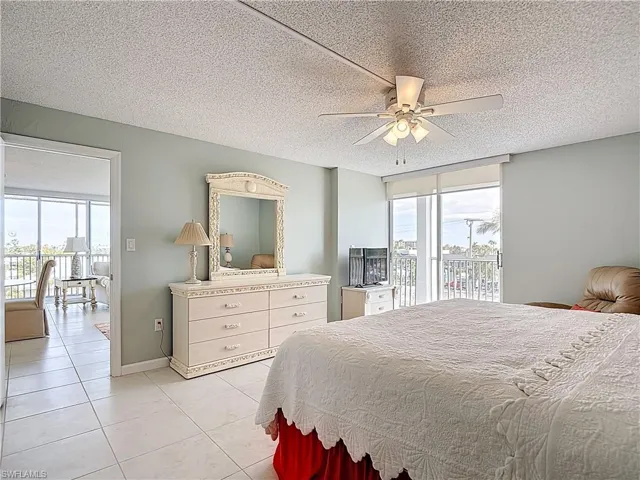 Bedroom featuring a textured ceiling, access to outside, light tile patterned floors, multiple windows, and ceiling fan