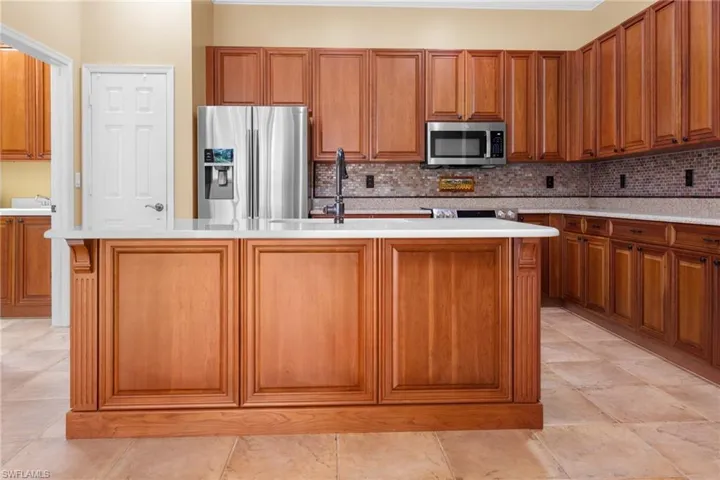 Kitchen with appliances with stainless appliances, backsplash, light tile patterned floors, and a kitchen island with sink.