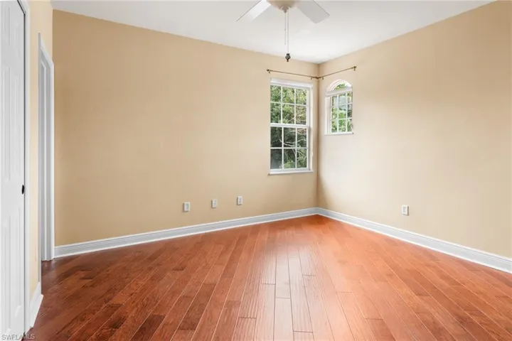 Guest bedroom 1 featuring ceiling fan and wood flooring, impact windows.