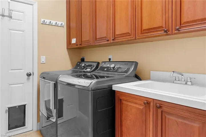 Laundry room with separate washer and dryer, cabinets, and sink.