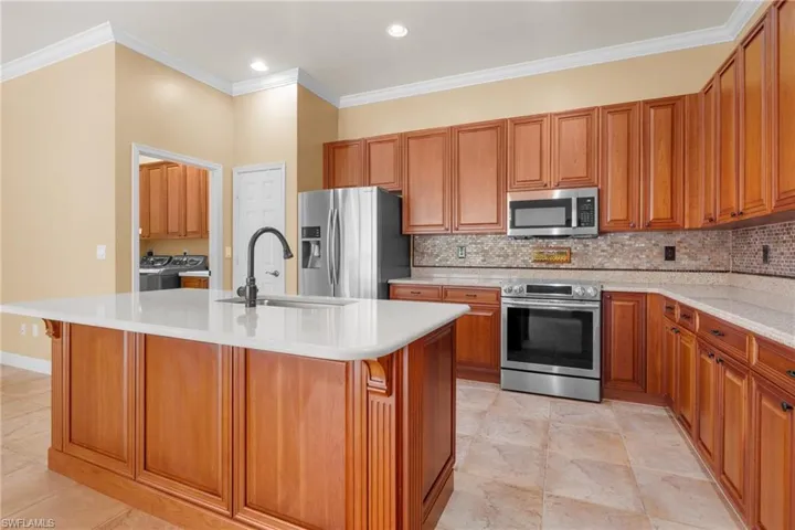 Kitchen featuring stainless appliances, light tile patterned floors, an island with sink, and tasteful backsplash.