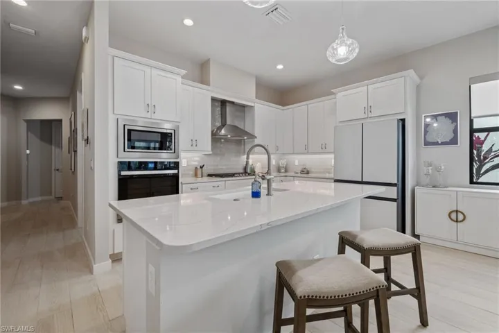 Kitchen with wall chimney exhaust hood, light wood-type flooring, white cabinets, and stainless steel appliances