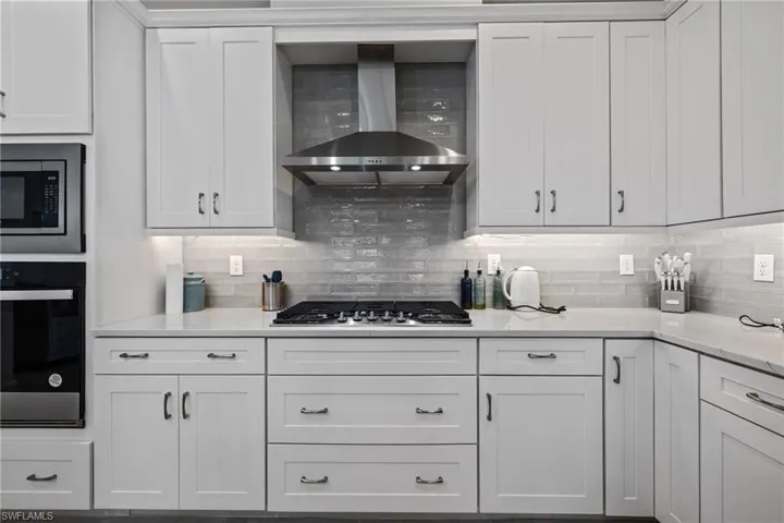 Kitchen featuring light stone counters, stainless steel appliances, backsplash, white cabinetry, and wall chimney range hood