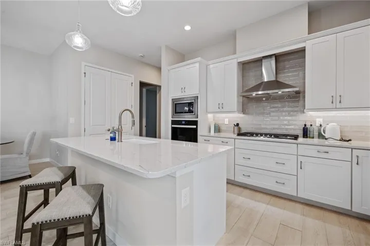 Kitchen featuring stainless steel appliances, a breakfast bar, a sink, wall chimney range hood, and backsplash