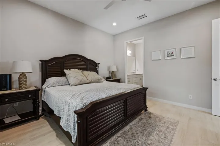 Bedroom with ensuite bathroom, light wood finished floors, visible vents, and baseboards