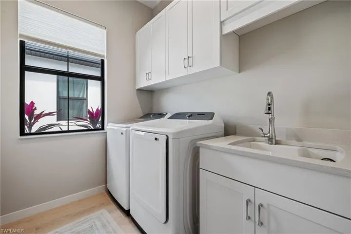 Laundry room featuring washing machine and dryer, light wood-style flooring, a sink, baseboards, and cabinet space