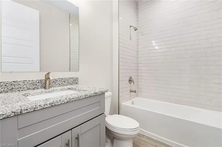 Full bathroom with toilet, large vanity, and tiled shower / bath