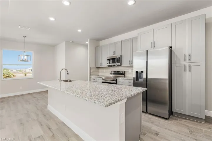 Kitchen with decorative light fixtures, tasteful backsplash, a kitchen island with sink, appliances with stainless steel finishes, and sink