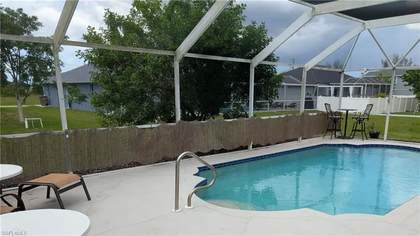 Screened-in outdoor living space featuring an in-ground swimming pool with blue tile trim, a concrete pool deck, and a bamboo privacy screen