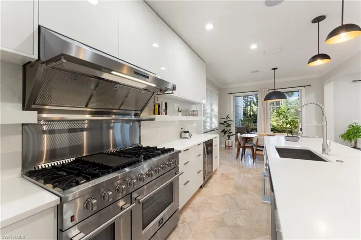 Kitchen featuring decorative light fixtures, light stone counters, white cabinetry, crown molding, and range with two ovens