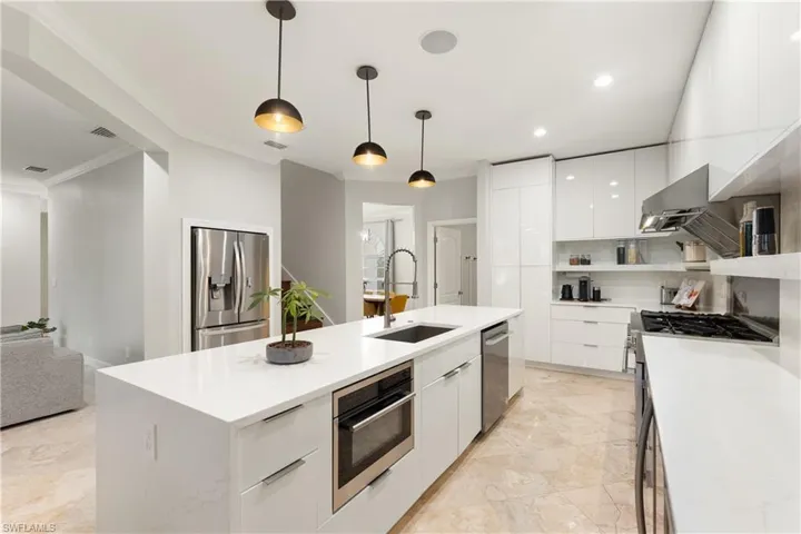 Kitchen featuring modern cabinets, hanging light fixtures, appliances with stainless steel finishes, white cabinets, and a center island with sink