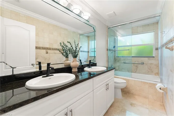 Bathroom with double vanity, tiled shower / bath, crown molding, tile walls, and light tile patterned floors