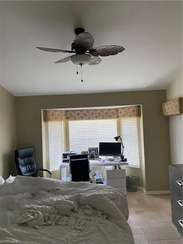 Bedroom featuring a desk, a ceiling fan, and stone tile floors