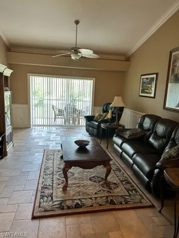 Living room featuring a wainscoted wall, a decorative wall, ceiling fan, ornamental molding, and stone tile floors