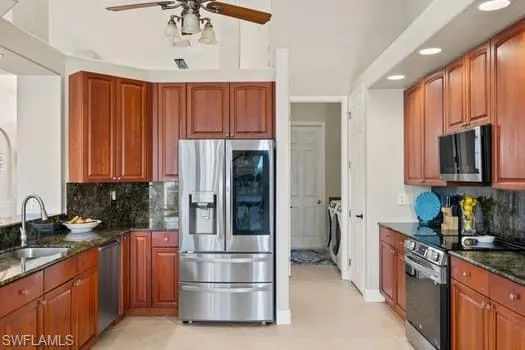 Kitchen with sink, backsplash, dark stone counters, independent washer and dryer, and stainless steel appliances
