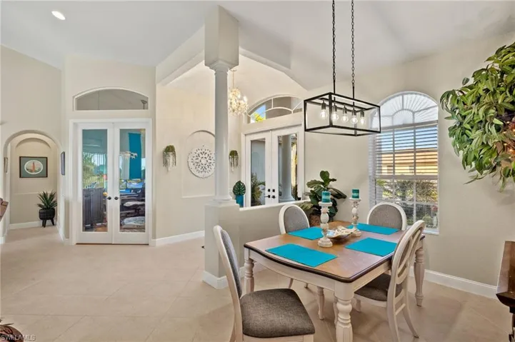 Dining room featuring lofted ceiling, light tile patterned floors, decorative columns, french doors, and a chandelier
