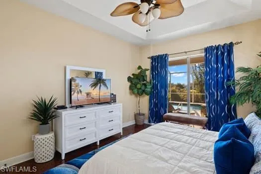 Bedroom with dark hardwood / wood-style floors, ceiling fan, a tray ceiling, and access to outside