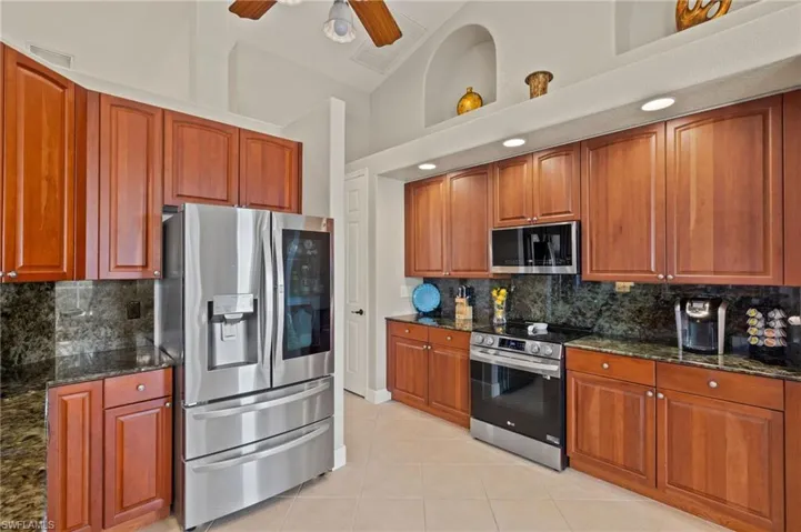 Kitchen with appliances with stainless steel finishes, dark stone countertops, decorative backsplash, and light tile patterned floors