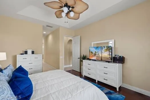 Bedroom featuring a raised ceiling, dark hardwood / wood-style floors, and ceiling fan