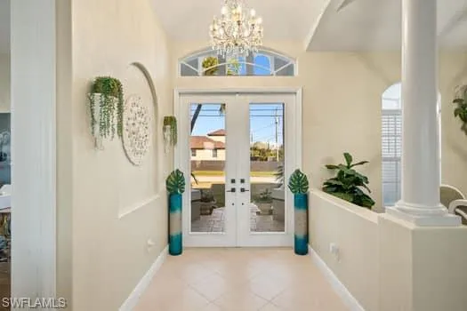 Doorway featuring lofted ceiling, light tile patterned floors, decorative columns, french doors, and a chandelier