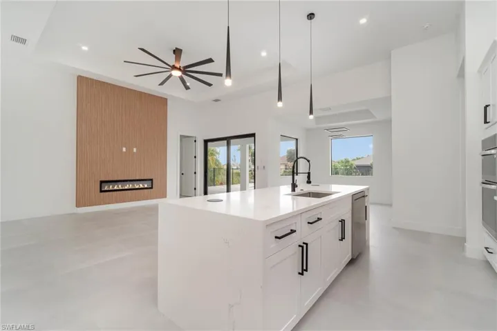 Kitchen with a raised ceiling, sink, white cabinetry, and an island with sink