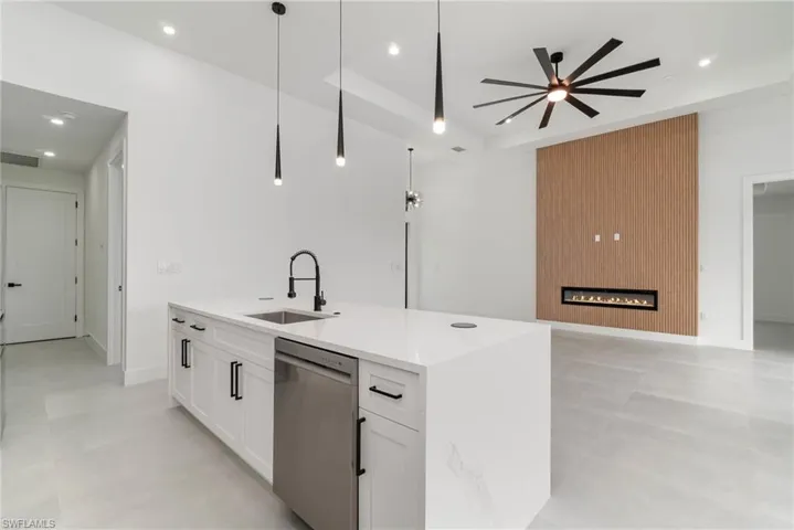 Kitchen with a large fireplace, white cabinetry, ceiling fan, sink, and dishwasher